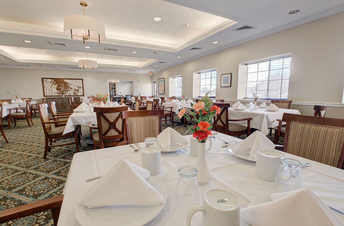 A well-lit dining room with tables set with white tablecloths and neatly arranged napkins.