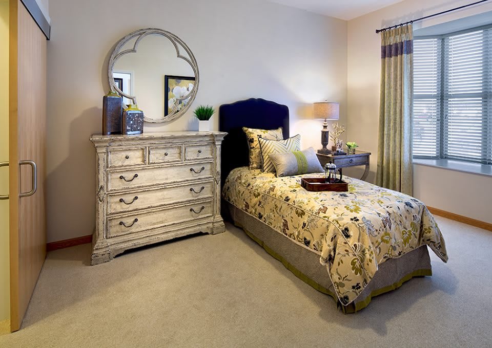 A cozy bedroom with a single bed, vintage dresser, and decorative mirror.