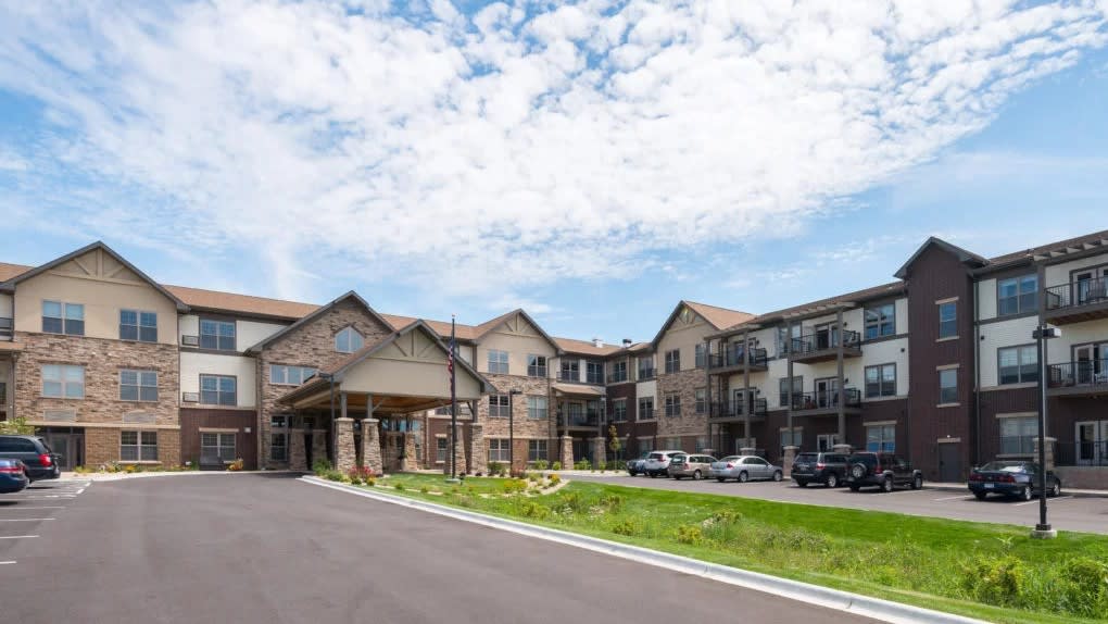A suburban apartment building with a parking lot under a partly cloudy sky.