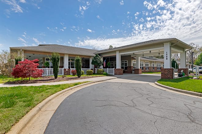 A large building with a driveway leading to its entrance, surrounded by well-maintained landscaping under a partly cloudy sky.