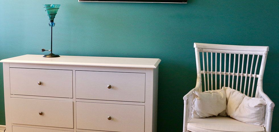 A cozy corner featuring a white chest of drawers and a matching chair against a teal-colored wall.