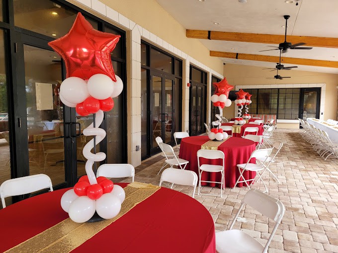 An outdoor party setup with red and white balloon decorations, tables, and chairs.