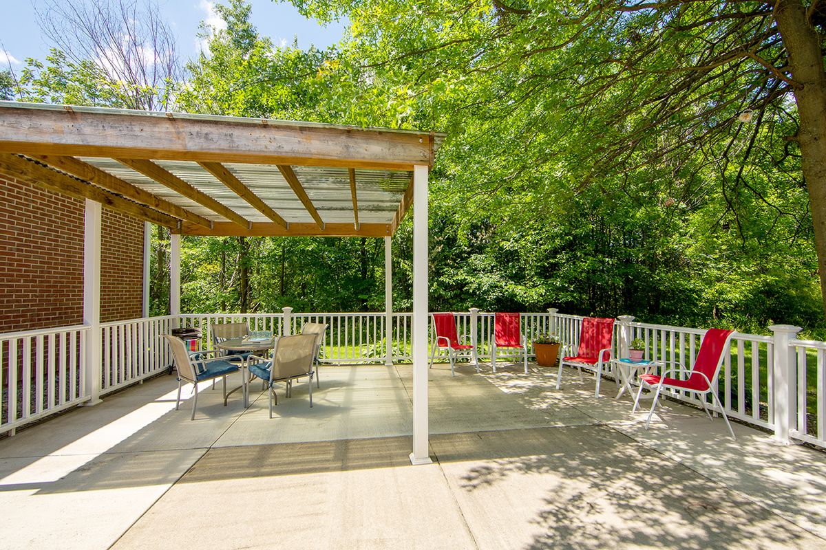 A sunny outdoor deck with a covered seating area and lush trees in the background.
