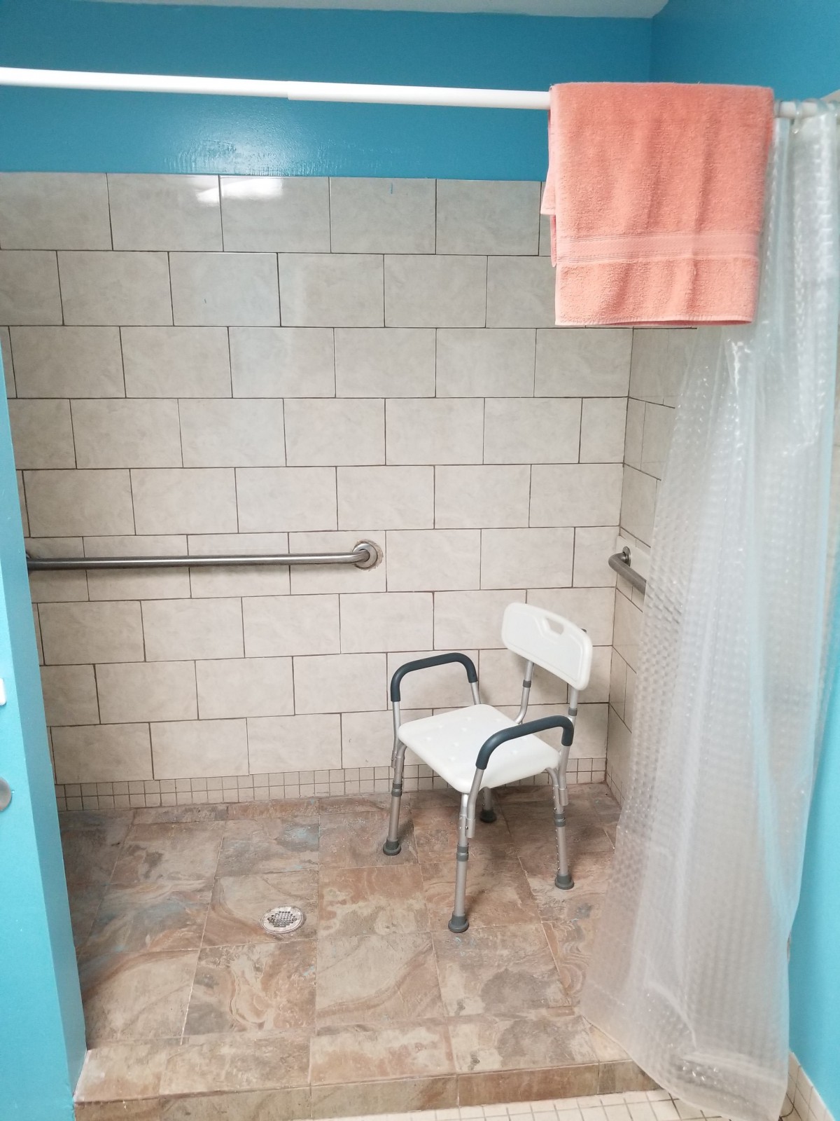 An accessible shower with a chair and grab bar, featuring tiled walls and a towel hanging.
