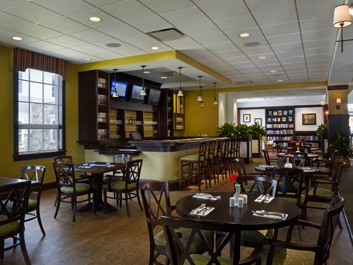 A modern restaurant interior featuring a dining area with tables, chairs, and a bar equipped with TV screens.
