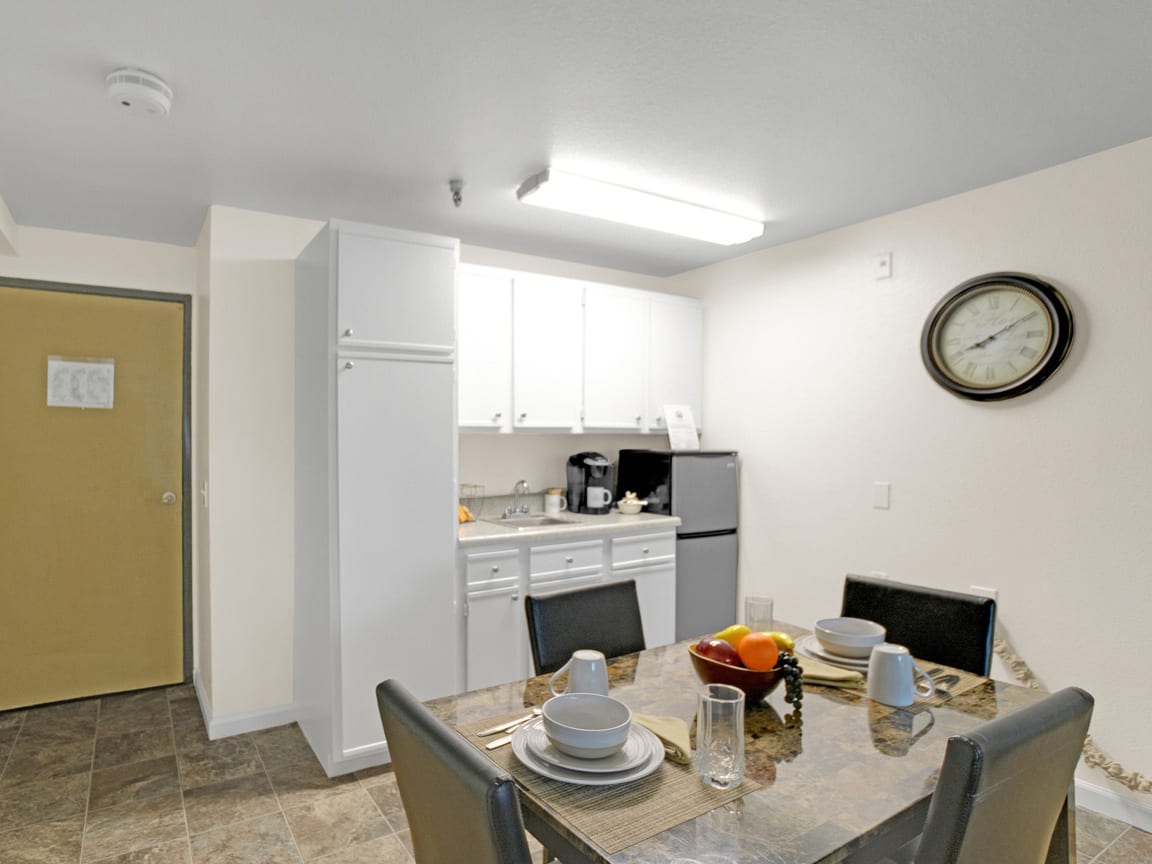 A modern kitchen and dining area with a fully set dining table, appliances, and a wall clock.