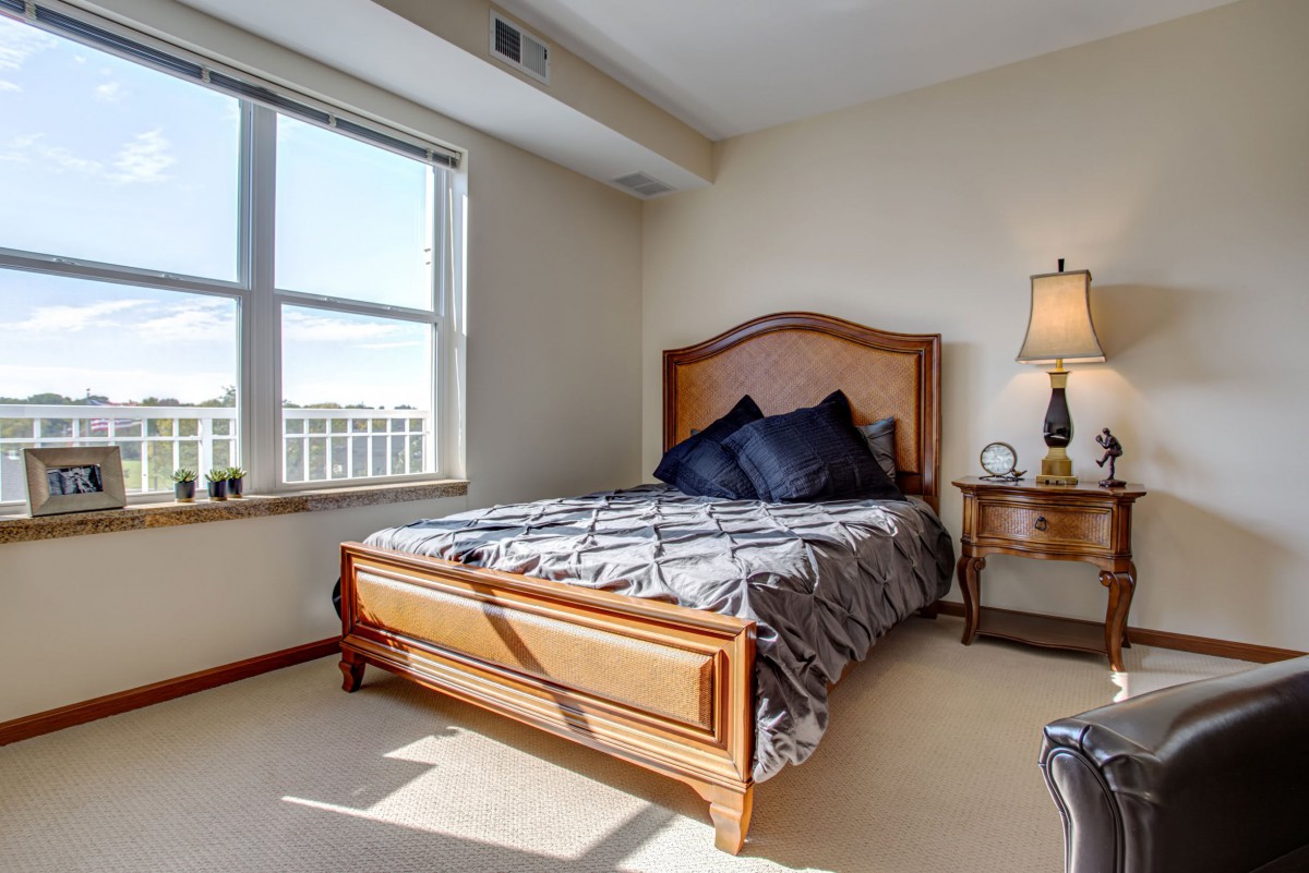 A cozy bedroom with a wooden bed frame, bedside table, and large window.