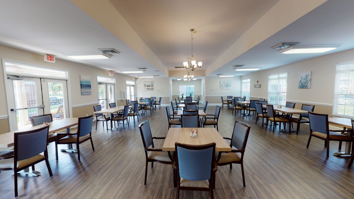 A spacious dining room with multiple tables and chairs, featuring large windows and elegant lighting.
