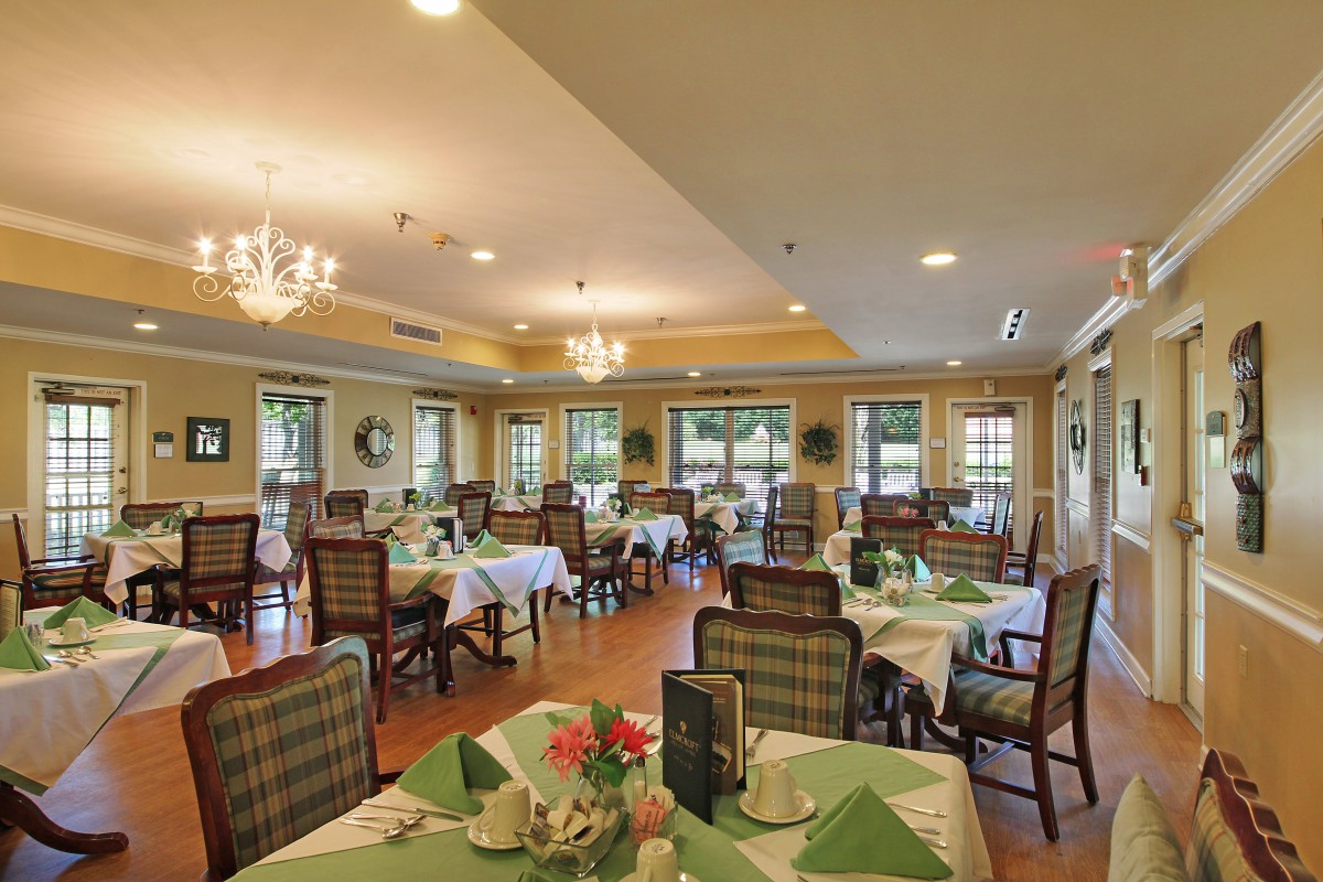 A well-decorated dining room with neatly arranged tables and chairs, featuring elegant chandeliers and large windows.
