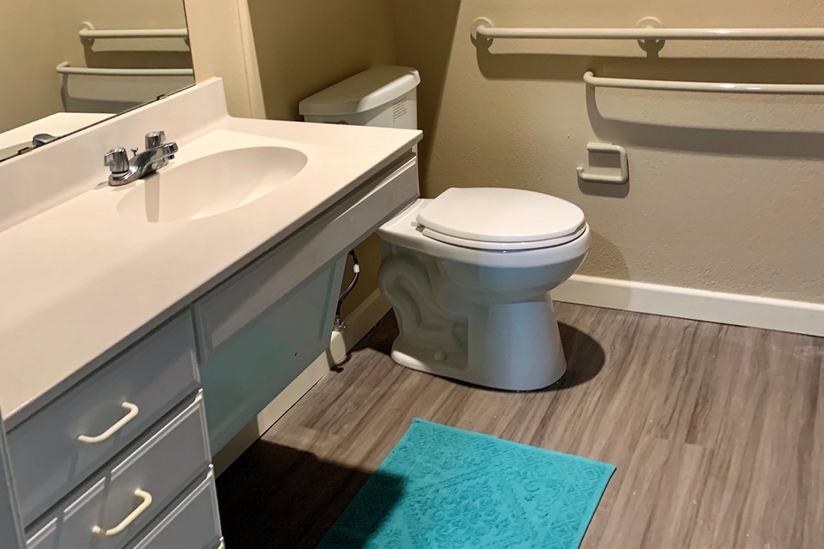 A clean and accessible bathroom with a toilet, sink, and teal mat.