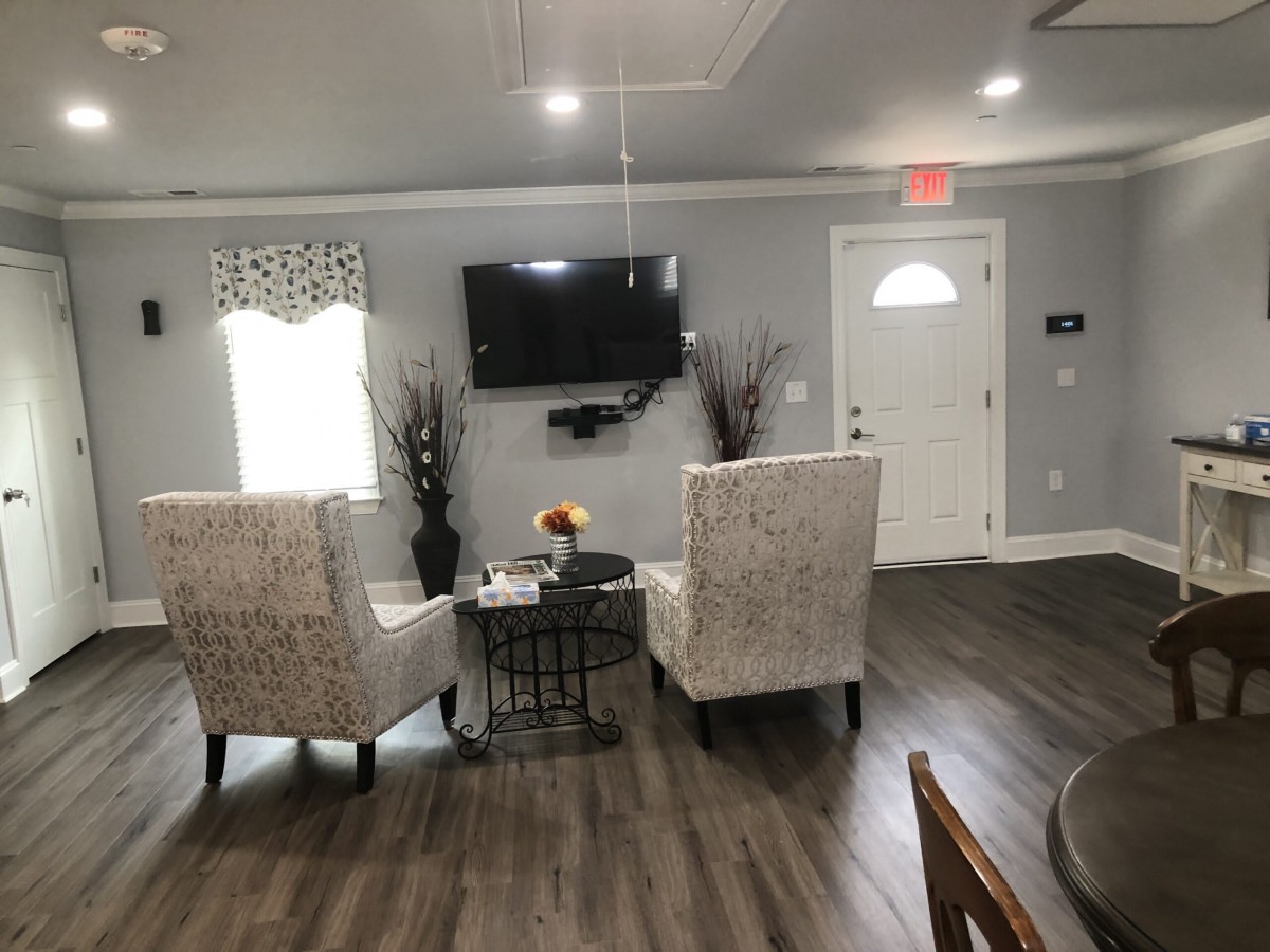 A modern living room with two upholstered chairs, a mounted television, and wood flooring.