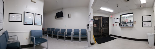 An empty hospital waiting room with blue chairs and a television mounted on the wall.