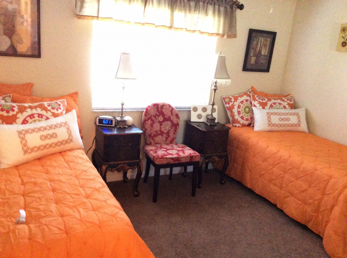A cozy bedroom with two twin beds featuring orange bedding, a chair between them, and lamps on side tables.