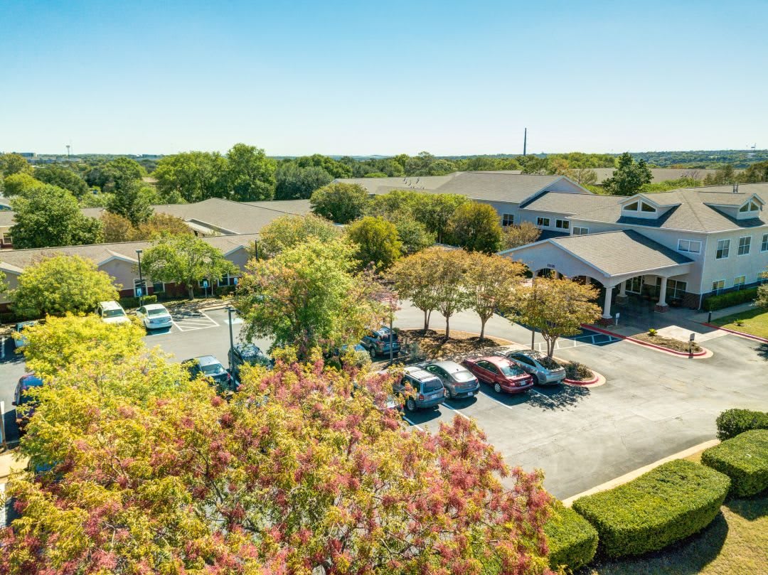 Aerial view of a building complex with a parking lot surrounded by trees.