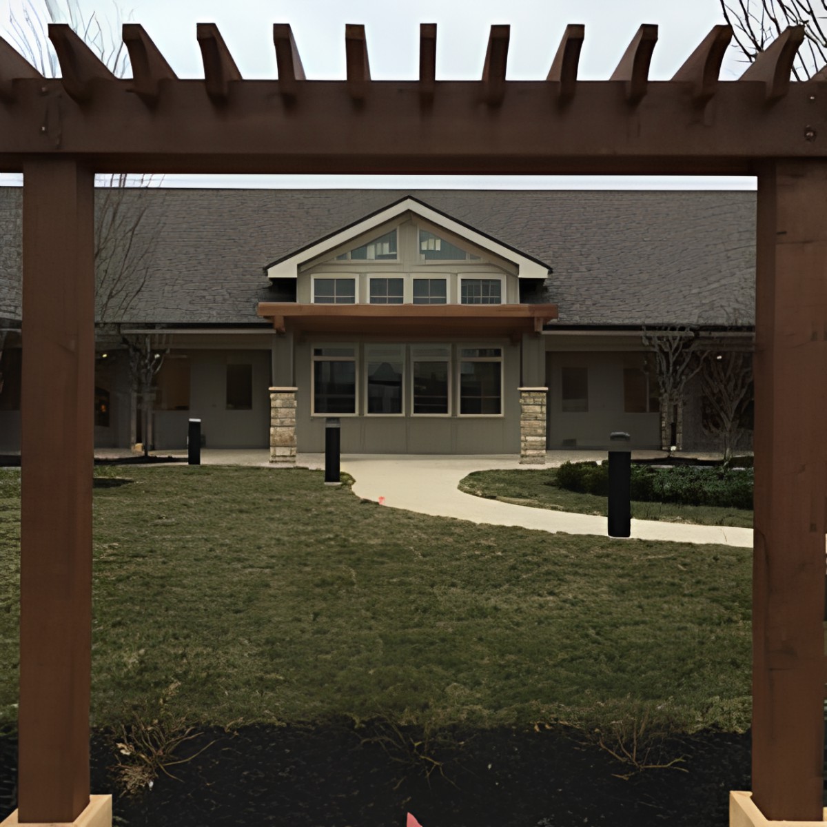 A suburban house framed by a wooden pergola, with a neatly manicured lawn and pathway leading to the entrance.