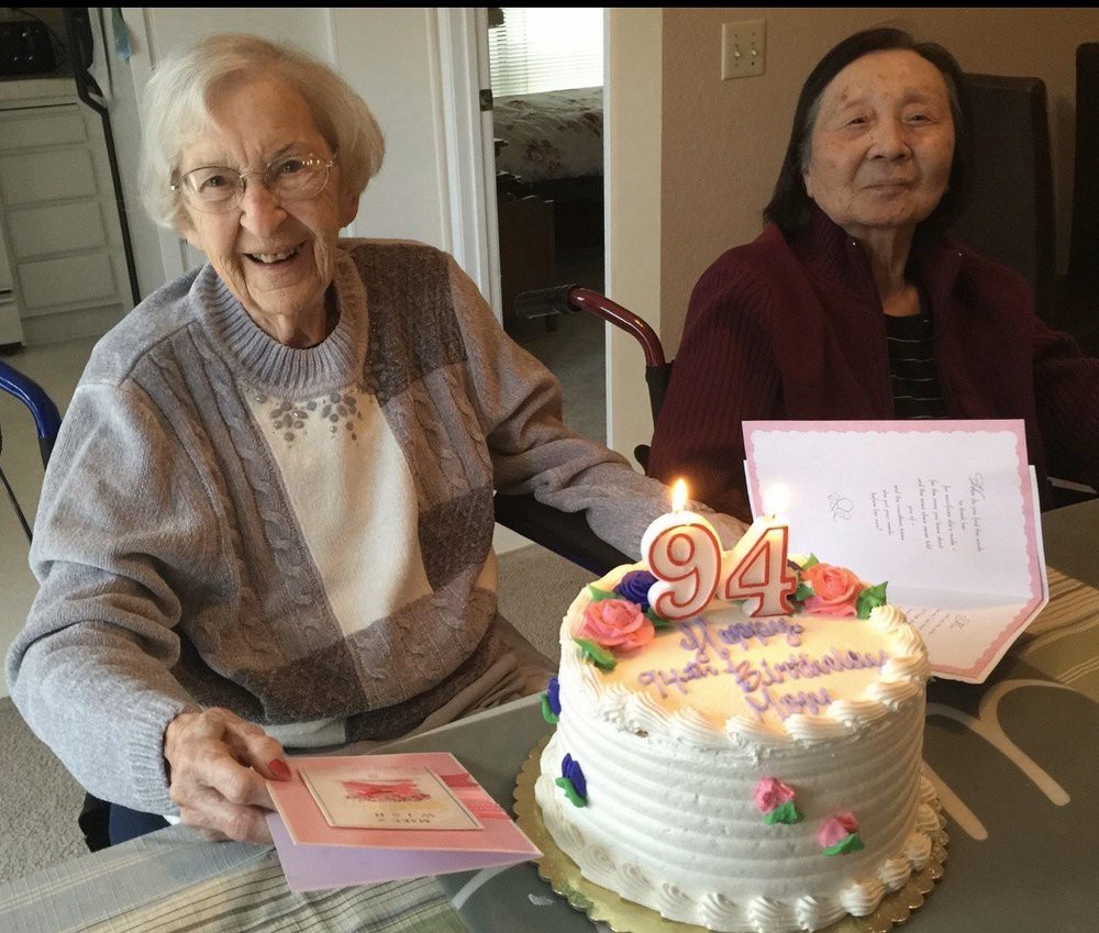 Two elderly women celebrating a birthday with a decorated cake and cards.