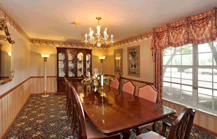 A formal dining room with a large wooden table, surrounded by upholstered chairs and adorned with a chandelier.