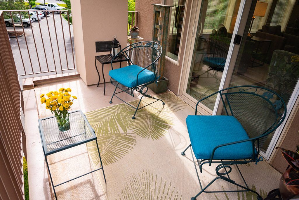 A cozy balcony setup with blue-cushioned chairs and a small table adorned with yellow flowers.