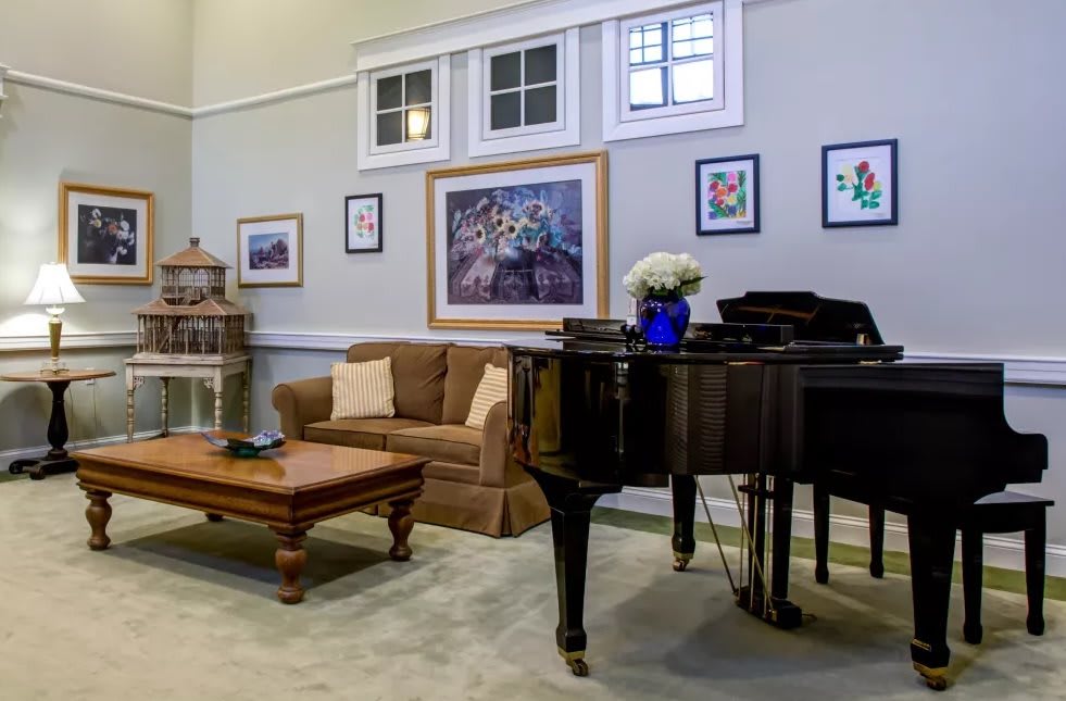 A cozy living room featuring a grand piano, comfortable couch, and various artworks on the walls.
