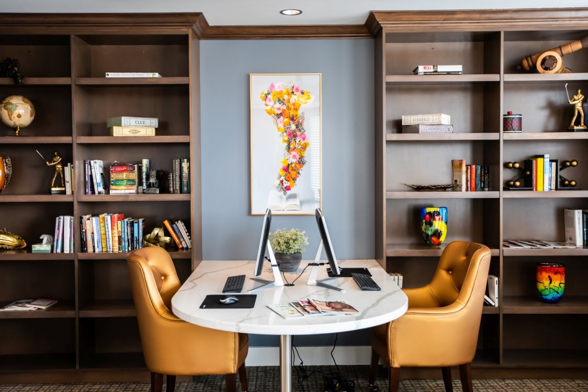 A cozy office space with a round desk, two leather chairs, and bookshelves filled with books.