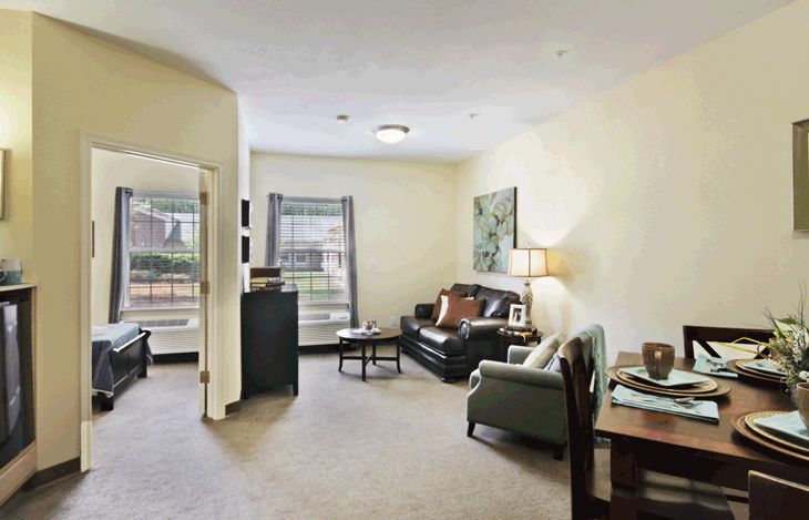 A cozy living room with modern furniture, featuring a sofa, armchair, and a lamp by the window.