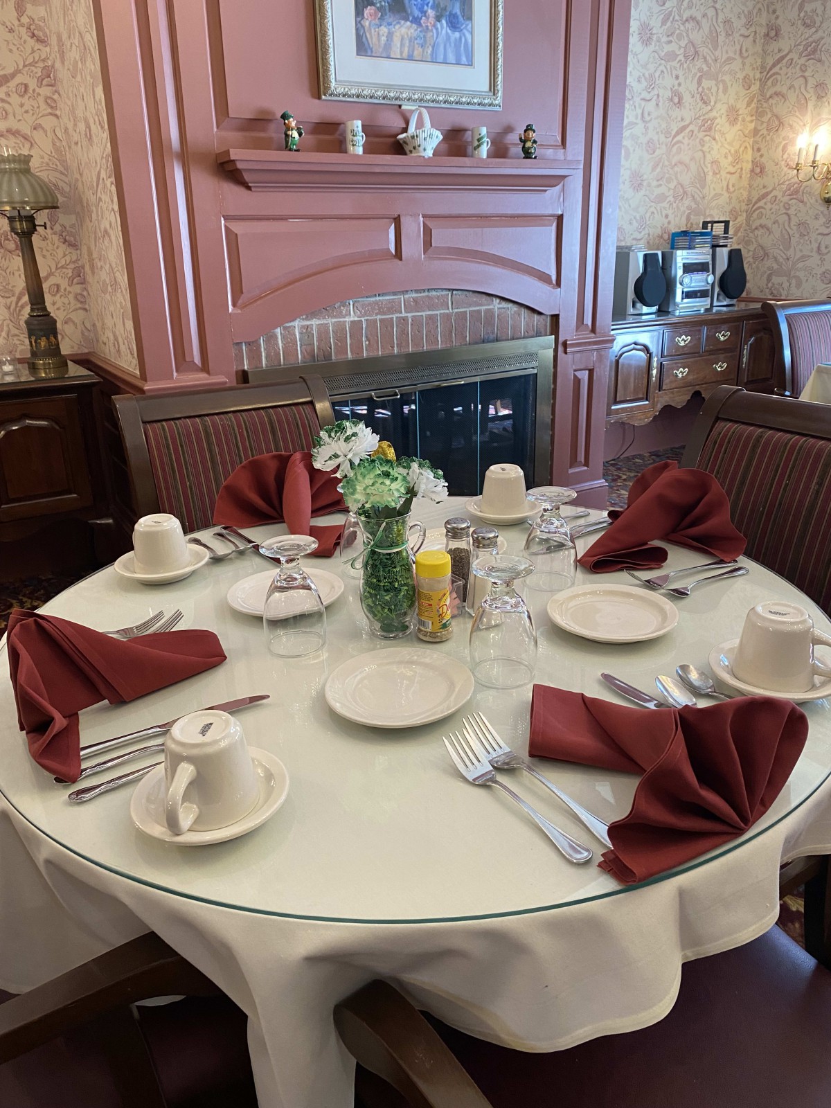 A formally set round dining table with red napkins, white dishes, and a floral centerpiece.