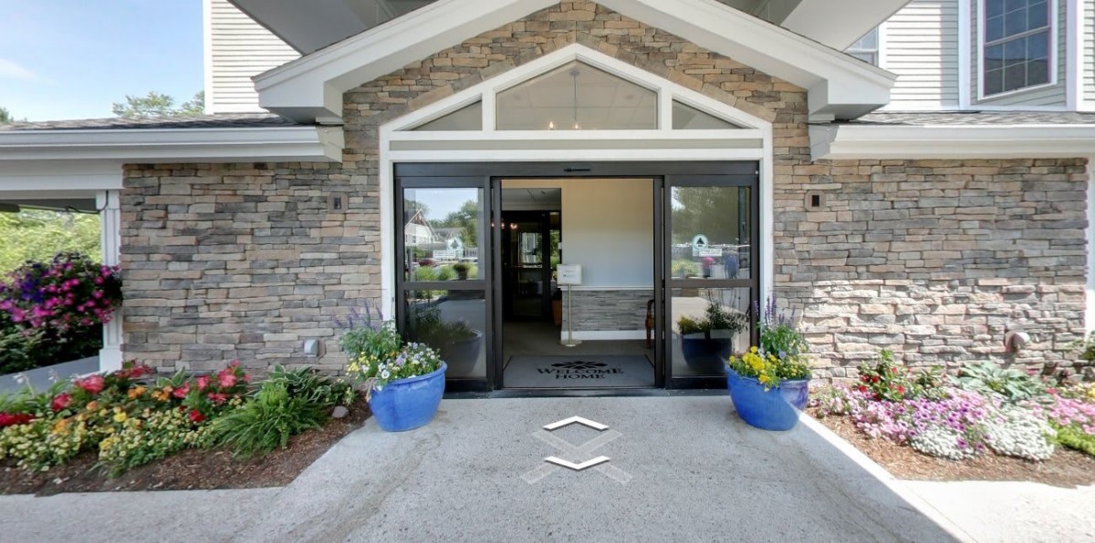 A building entrance with stone walls, glass doors, and potted plants on either side.