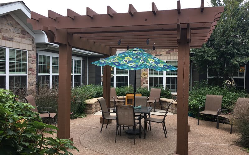 A cozy patio setup featuring a pergola, table, chairs, and a colorful umbrella.