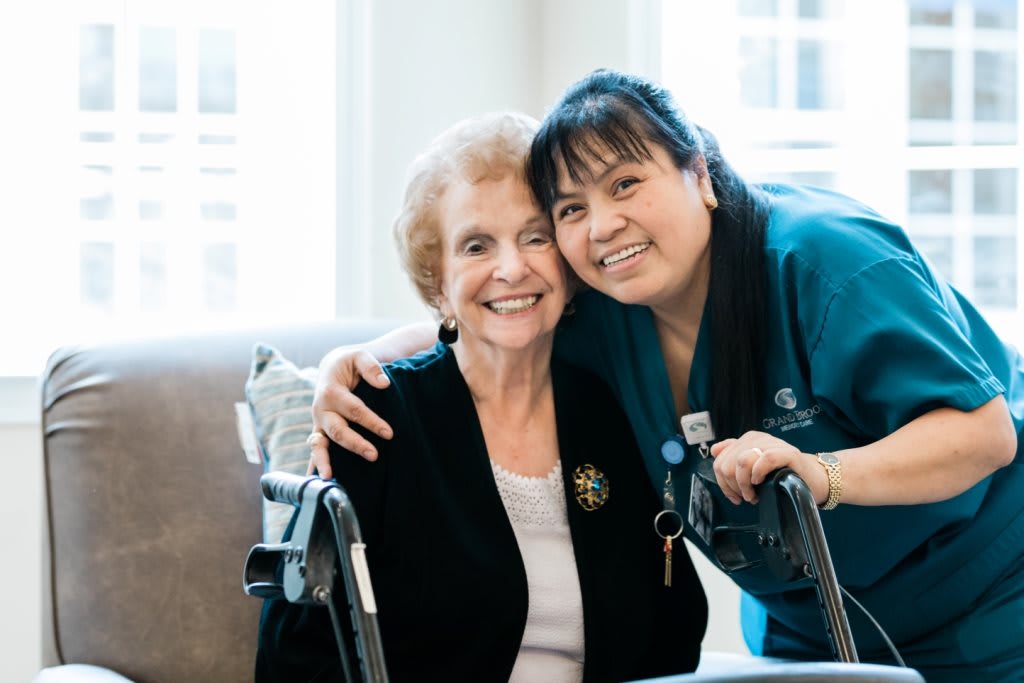 An elderly woman and her caregiver share a warm embrace, smiling together.