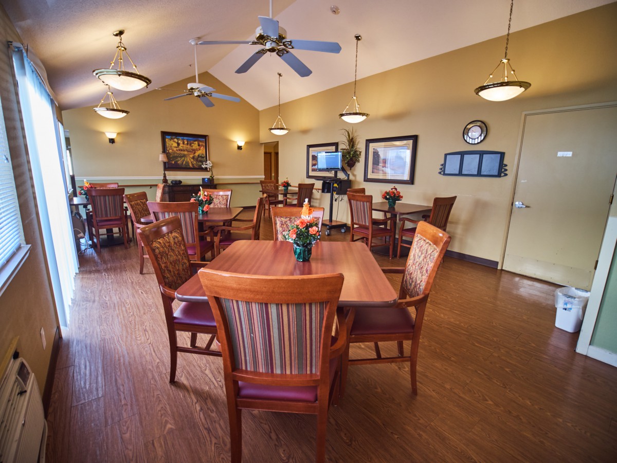 An inviting dining area featuring wooden tables and chairs, with warm lighting and a ceiling fan.
