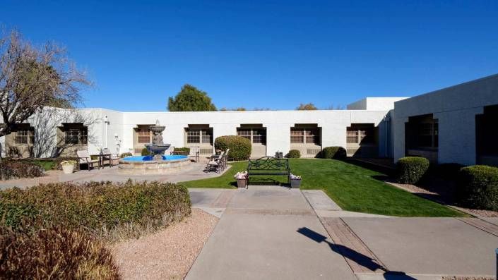 A landscaped courtyard with benches, a fountain, and a modern building under a clear blue sky.