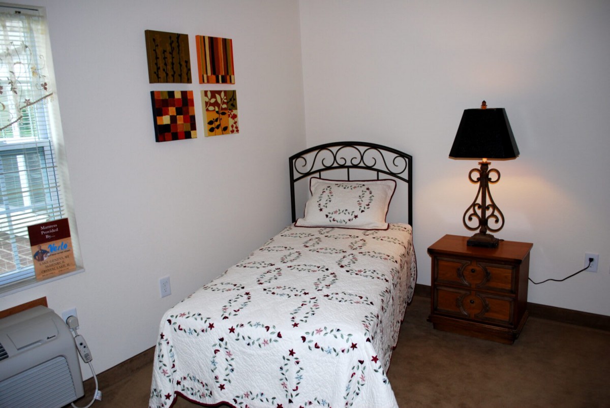 A small bedroom with a single bed, decorative wall art, and a nightstand with a lamp.