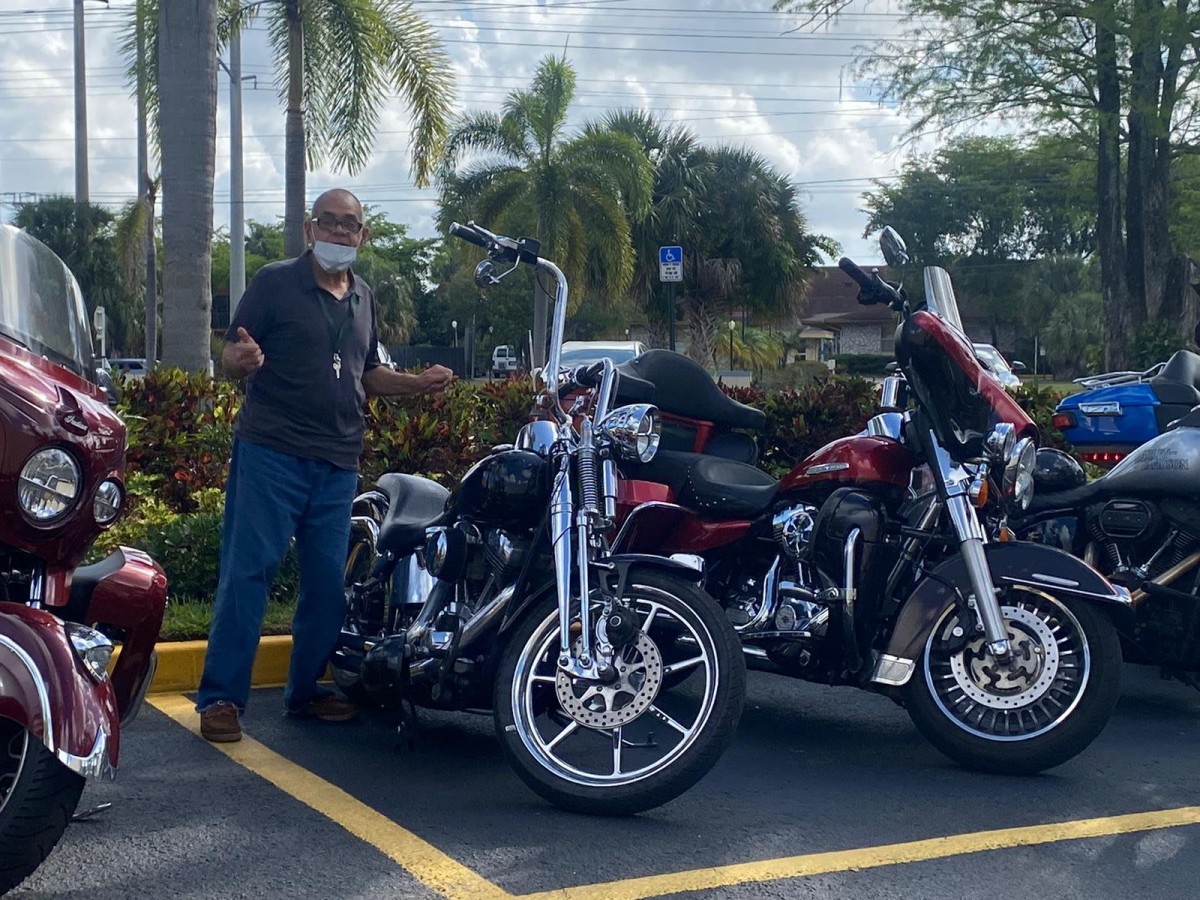 A person stands next to two parked motorcycles in a parking lot on a sunny day.
