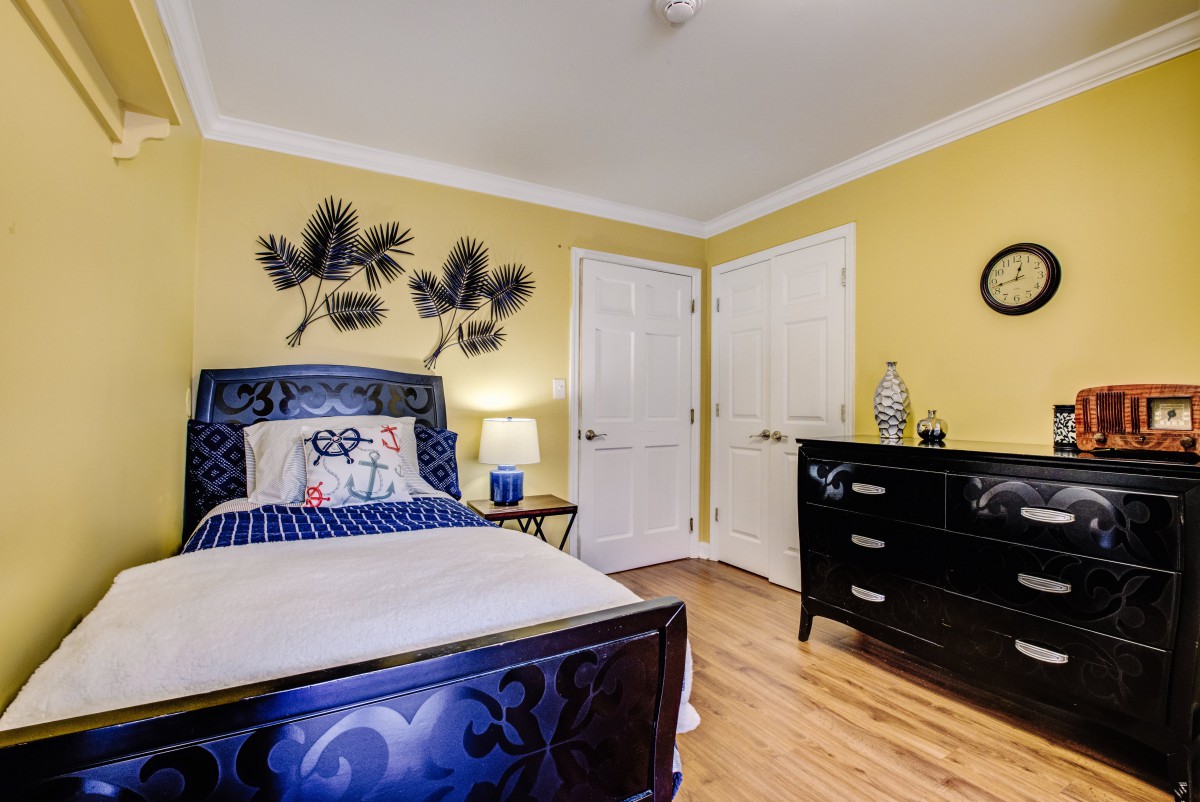 A cozy bedroom with yellow walls, featuring a single bed, decorative wall art, and a dresser on a wooden floor.