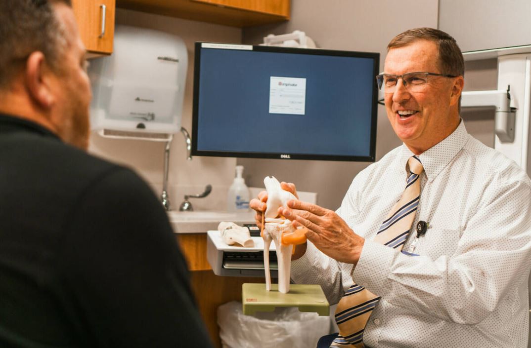 A doctor explains a knee model to a patient during a medical consultation in an office setting.