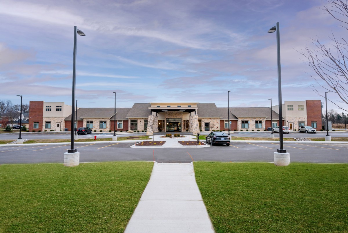 A modern building with a parking lot and neatly landscaped surroundings under a cloudy sky.