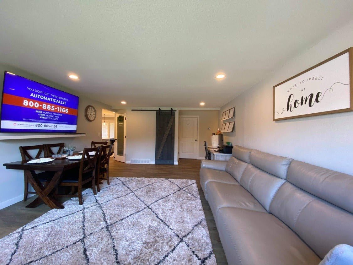 A modern living room featuring a large sofa, wall-mounted television, dining table, and stylish decor.
