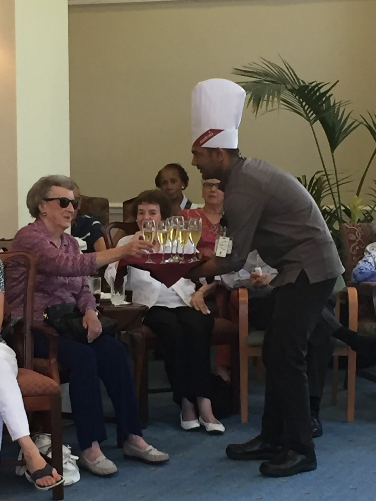 A chef presents a cake to an elderly woman during a celebration indoors.
