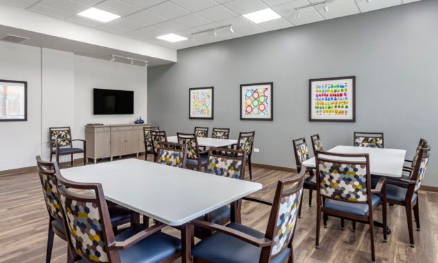 A modern meeting room with tables, chairs, artistic decor, and a TV on the wall.