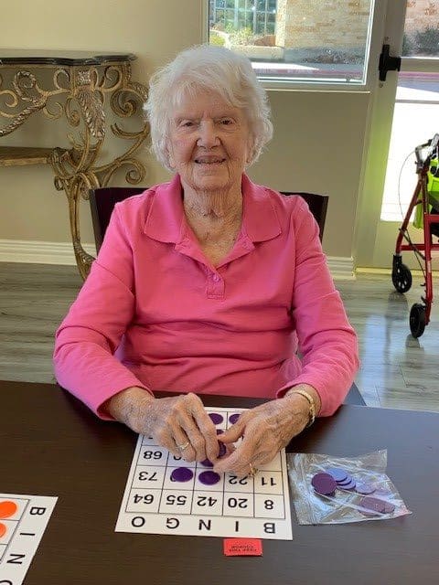 An elderly woman in a pink shirt playing bingo indoors.