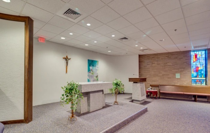 A small chapel with an altar, cross, and lectern, decorated with plants.