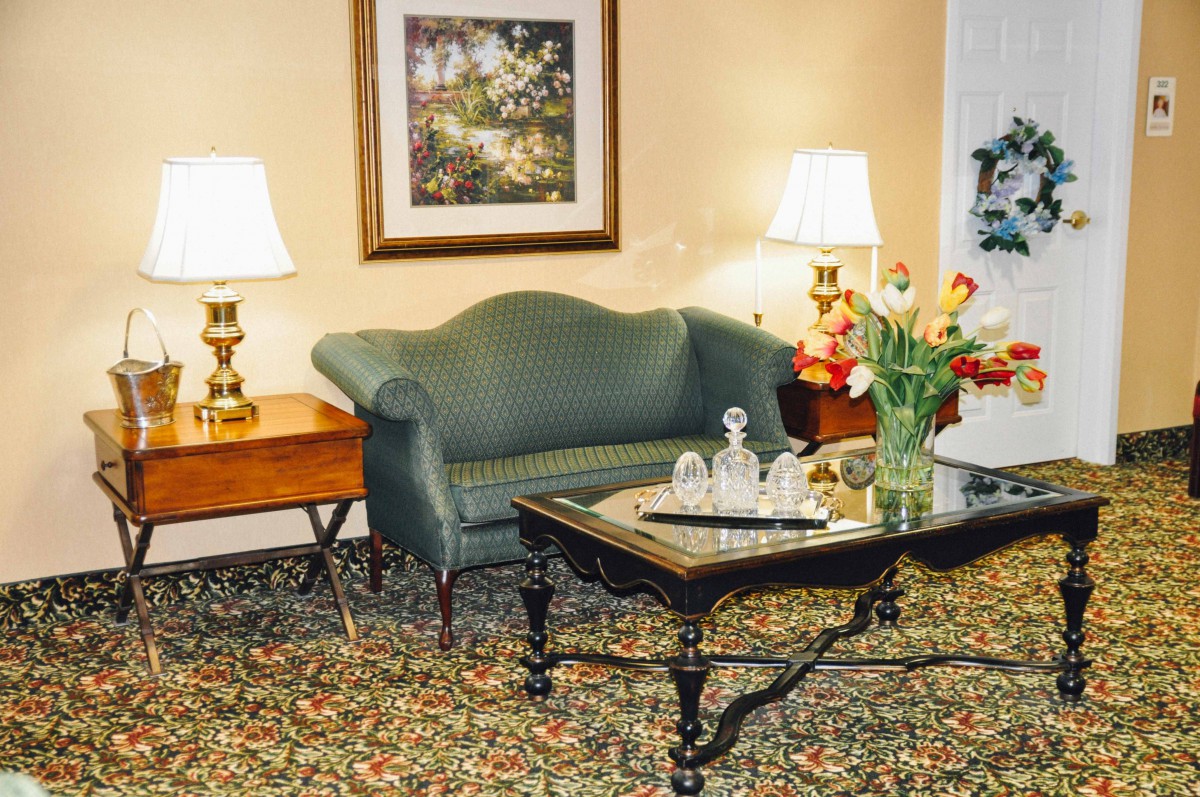 A cozy living room with a green sofa, wooden table, and decorative elements like lamps and flowers.