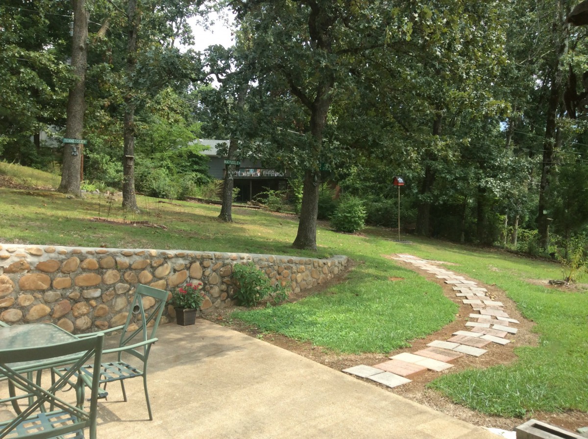 A serene outdoor garden with a stone pathway leading through lush greenery and trees.