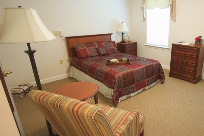 A cozy bedroom featuring a bed with patterned bedding, a lamp on the nightstand, and a striped armchair.