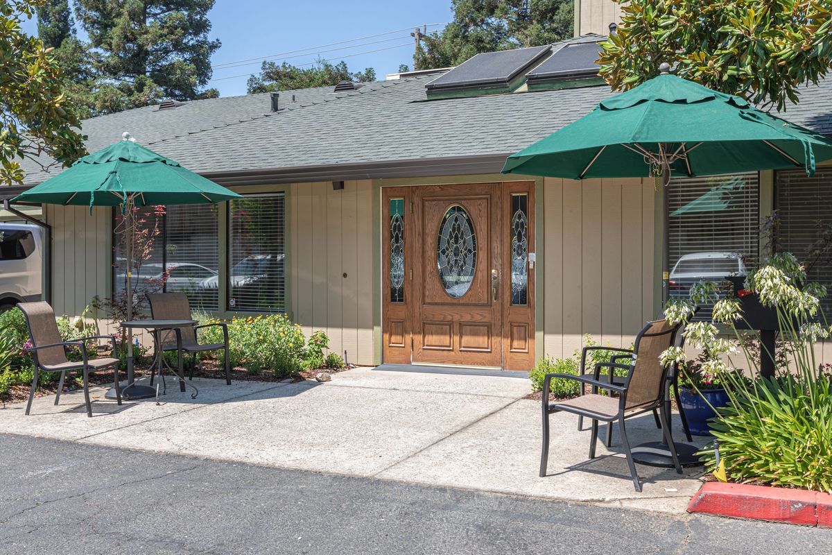 A cozy building entrance with outdoor seating and green umbrellas.