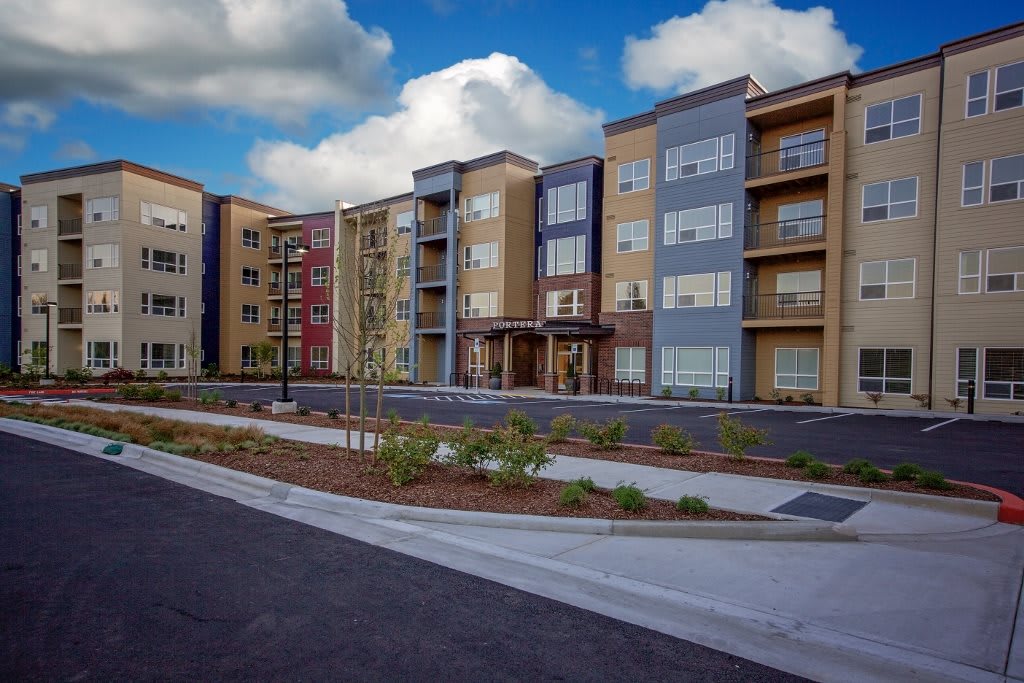 A modern multi-story apartment building with well-maintained landscaping under a blue sky.