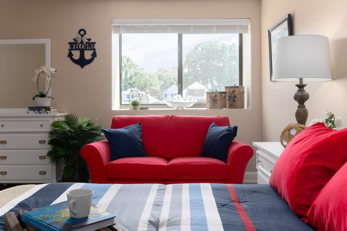 A cozy living space featuring a bright red sofa with blue cushions, nautical decorations, and a striped bedspread.