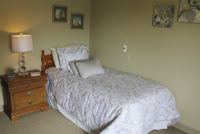 A cozy bedroom with a single bed, pillow, and a wooden nightstand.