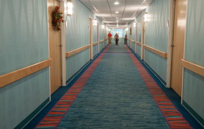 A brightly lit hotel hallway with patterned carpet and doors on each side.
