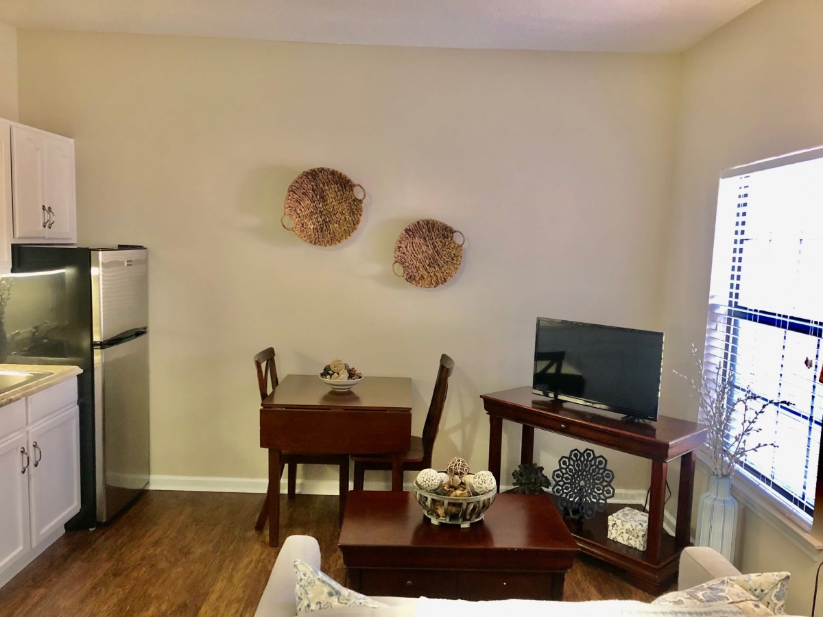 A cozy living room with minimalist decor, featuring a small dining table set and a TV on a wooden stand.